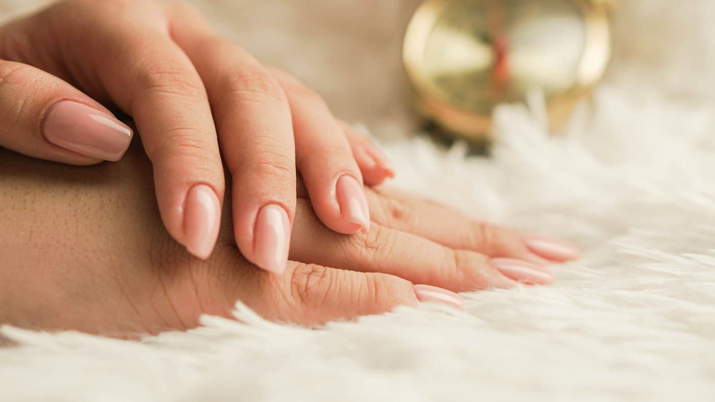 Mãos com esmaltação nude repousando sobre manta felpuda
