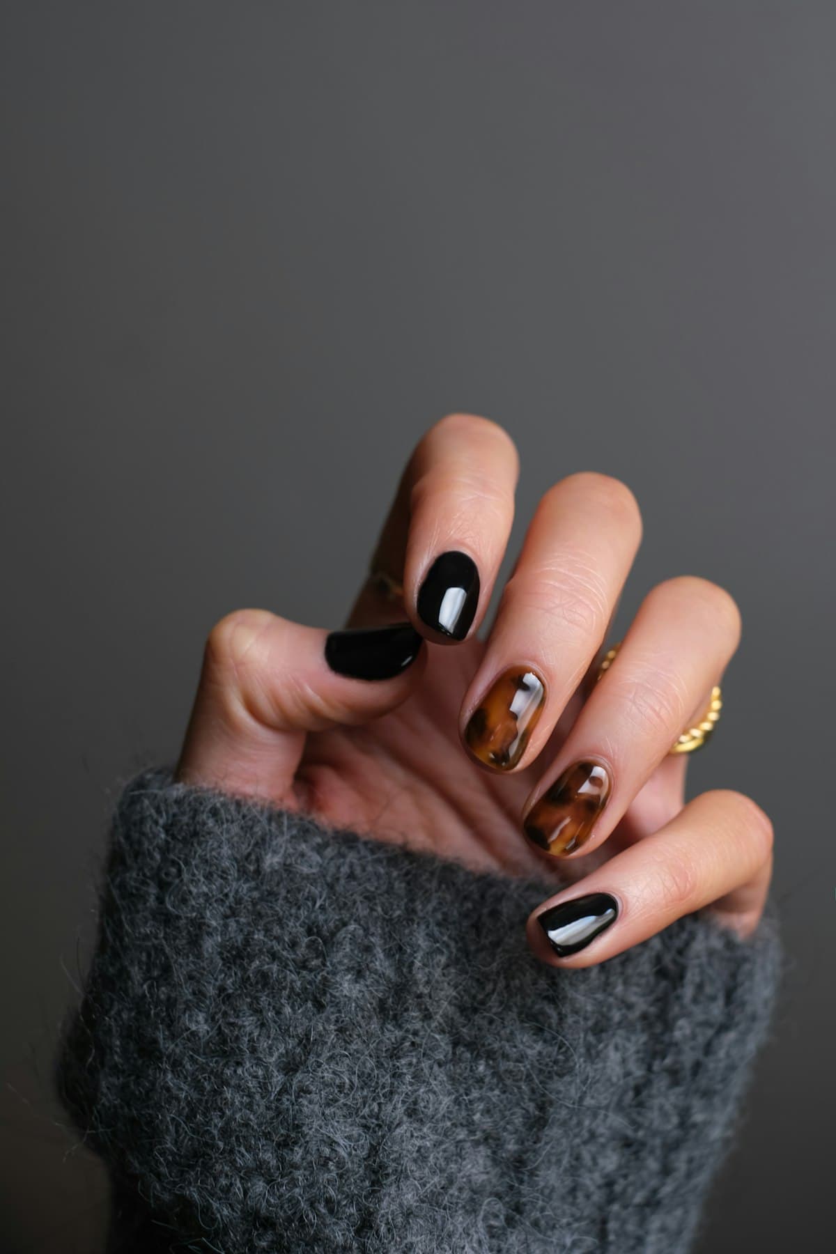 Mão com unhas em esmalte preto e detalhes em dourado sobre tricô cinza