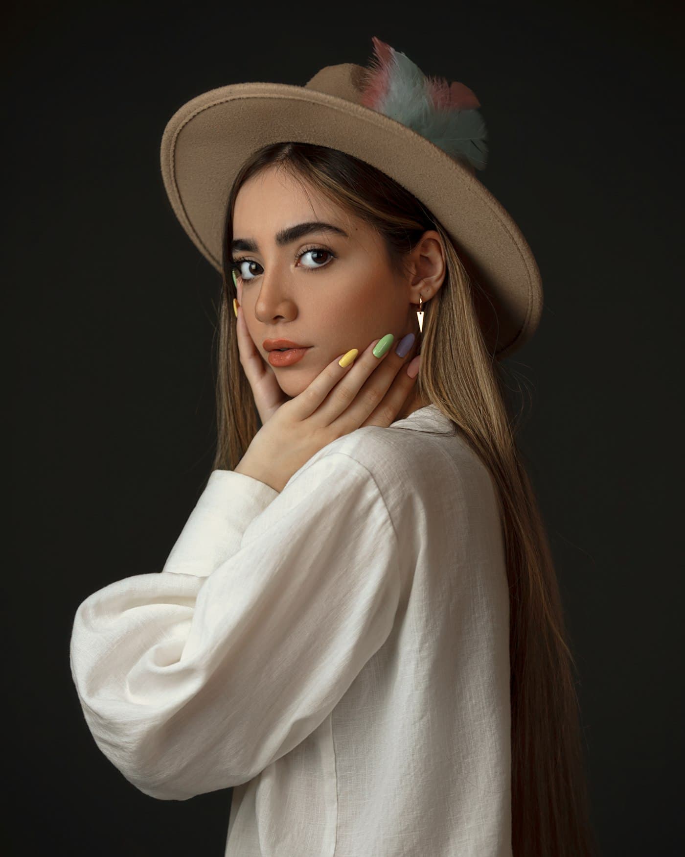 Mulher de chapéu e blusa off-white em retrato editorial com fundo escuro